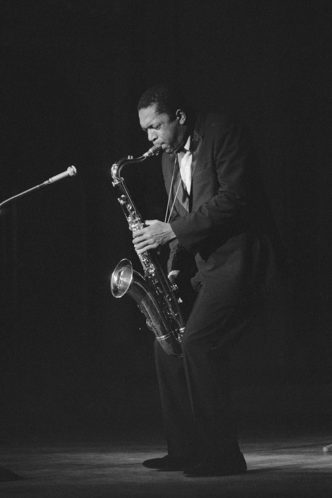 Black and white photo of a saxophonist playing on stage with a microphone.